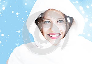 Christmas and winter holiday portrait of young woman in white hooded fur coat, snow on blue background, fashion and