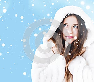 Christmas and winter holiday portrait of young woman in white hooded fur coat, snow on blue background, fashion and