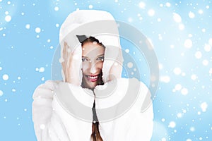 Christmas and winter holiday portrait of young woman in white hooded fur coat, snow on blue background, fashion and