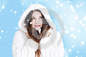 Christmas and winter holiday portrait of young woman in white hooded fur coat, snow on blue background, fashion and