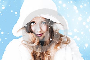 Christmas and winter holiday portrait of young woman in white hooded fur coat, snow on blue background, fashion and