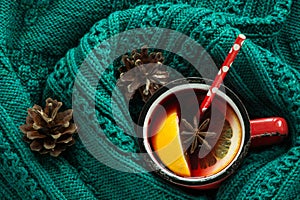 Christmas traditional hot beverage. Mulled wine in red mug with spice wrapped in warm green scandinavian sweater.