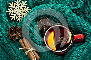 Christmas and winter traditional hot beverage. Mulled wine in red mug with spice wrapped in warm green sweater.