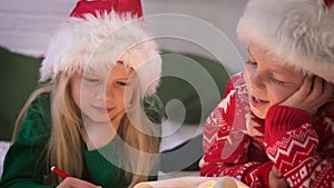 Christmas wish list. Smiling boy and girl in Santa Claus hat writing letter dreams for gifts to Santa Claus. Children