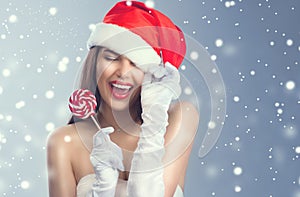 Christmas woman. Beauty model girl in Santa Claus hat with red lips and xmas lollipop candy in her hand. Joy. Surprised expression