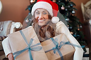 Christmas. Woman dressed white sweater Santa hat and jeans sitting on the floor near christmas tree with present box