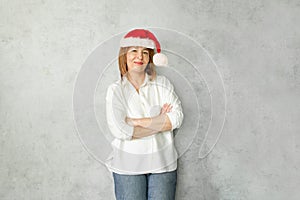 Christmas woman in red Santa hat against grey office wall background indoor