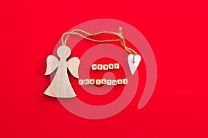 Christmas wooden angel with heart and twine with words Merry Christmas on little bricks on bright red background.