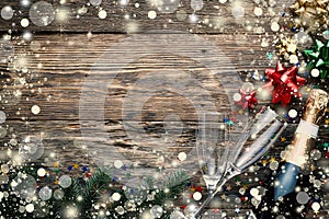 Christmas wooden background with falling snow, champagne, glasses, fluffy fir branches and festive decor, copy space for