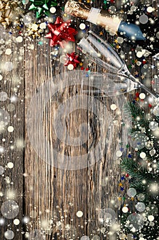 Christmas wooden background with falling snow, champagne, glasses, fluffy fir branches and festive decor, copy space for text, top