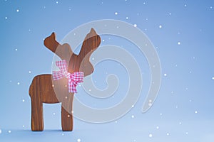 Christmas wooden deer on a blue background. Postcard with snowflakes effect