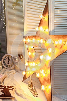 Christmas wooden star decoration with golden garland lights, white clock and shiny champagne glasses, pillow with reindeer illustr