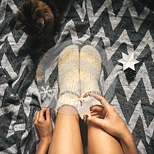 Christmas woolen socks on legs and woman holding stylish reindeer toy, and cute cat playing with holiday ornaments in festive