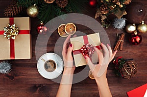 Christmas workplace top view. Girlâ€™s hands on the wooden table holding Christmas present. Christmas wreath, decorations