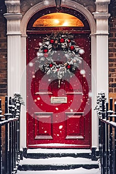 Christmas wreath and decoration on a classic red door on snowing winter holiday, Merry Christmas and Happy Holidays wishes,