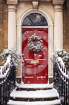 Christmas wreath and decoration on a classic red door on snowing winter holiday, Merry Christmas and Happy Holidays wishes,