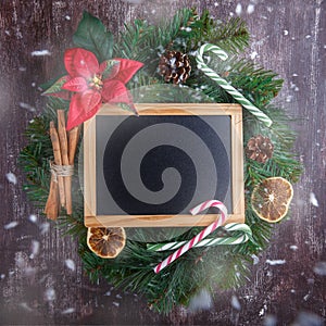 Christmas wreath with decorations and blank chalkboard with wooden frame on  wooden background.  New Year decoration. Top view,