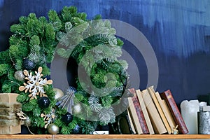 christmas wreath with decorations on shelf with books on blue background. Christmas, holidays and seasonal greetings concepts.