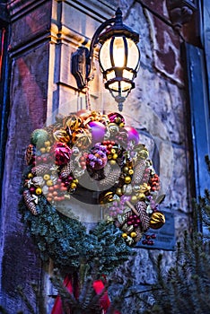 Christmas wreath on door under retro vintage lantern on Christmas eve in beautiful fairy tale lighting in european old town city.