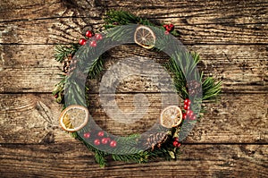 Christmas wreath of Fir branches, cones, red decoration on wooden background with snowflakes.