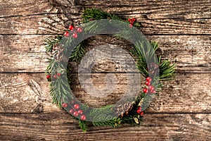 Christmas wreath of Fir branches, cones, red decoration on wooden background with snowflakes.