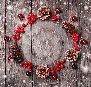 Christmas wreath of Fir branches, cones, red decorations on dark wooden background.