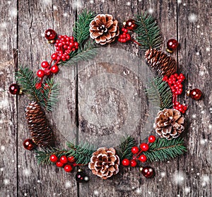 Christmas wreath of Fir branches, cones, red decorations on dark wooden background.