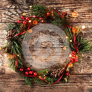 Christmas wreath of Fir branches, pine cones, berries and red ribbon on wooden background.