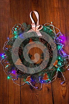 Christmas wreath flatlay. Green spruce decorated with orange zest, lights, pine cones and ribbon on wooden background
