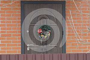 Christmas wreath hanging on a brown door on a red brick wall