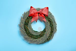 Christmas wreath made of fir branches with red bow on light blue background, top view