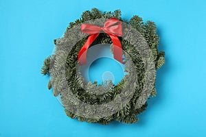 Christmas wreath made of fir tree branches with red ribbon on light blue background