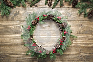 Christmas wreath made of spruce branches with holly berries on wooden board. Flat lay. Top view.