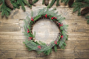 Christmas wreath made of spruce branches with holly berries on wooden board. Flat lay. Top view.