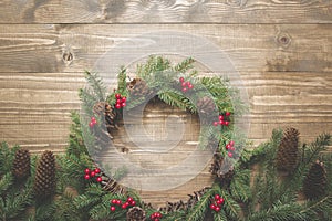 Christmas wreath of spruce branches with holly berries on wooden board. Flat lay. Top view. Toned image.