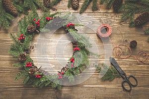 Christmas wreath made of spruce branches with holly berries on wooden board. Wreath workshop. Top view.