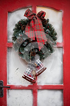 Christmas wreath with pine cones and red ribbon bow on on a red door.