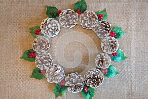 Christmas wreath of pinecones, holly leaves, and red berries on rustic fabric background