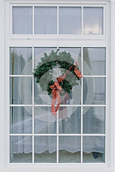 Christmas wreath with a red bow on a white window in a private house