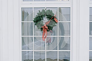 Christmas wreath with a red bow on a white window in a private house