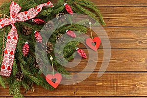 Christmas Wreath - red cones and red wooden hearts on green spruce branches on brown wooden background. Top down view