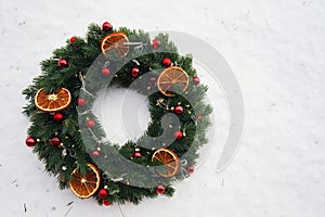 Christmas wreath with red spruce balls and dry citrus slices on a background of white snow