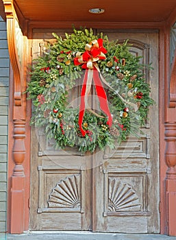 Christmas wreath with red and white bow, pine cones and red berries hanging on doors