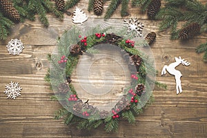 Christmas wreath of spruce branches with holly berries on wooden board. Flat lay. Top view.