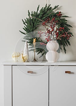 Christmas wreath on the wall, a vase with cranberry branches, a candle, Christmas toys on a white chest of drawers