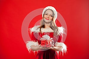 Christmas, x-mas, winter, happiness concept - smiling woman in santa helper hat with gift box, over red background