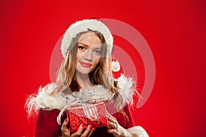 Christmas, x-mas, winter, happiness concept - smiling woman in santa helper hat with gift box, over red background