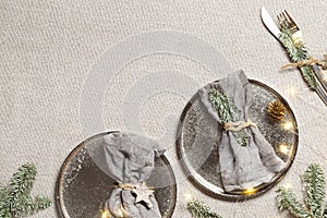 Christmas or Xmas dinner plate setting, linen napkin on metal plate, knife, fork with green fir branches on rustic