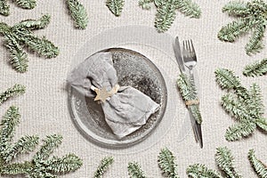 Christmas or Xmas dinner plate setting, linen napkin on metal plate, knife, fork with green fir branches on rustic