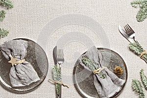 Christmas or Xmas dinner plate setting, linen napkin on metal plate, knife, fork with green fir branches on rustic